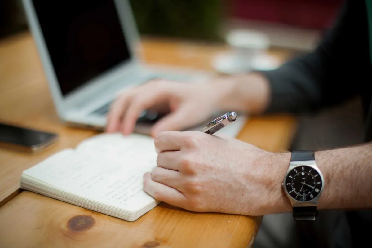 Demo photo: someone writing notes beside a laptop